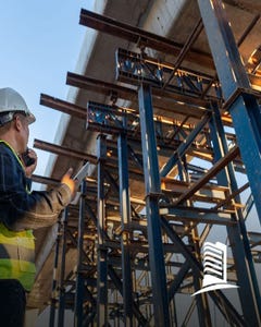 Engineer wearing a hard hat and safety vest talking on a walkie-talkie inspecting a steel structure.