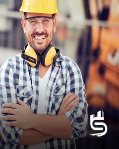 Man with a beard smiling wearing a hard hat and safety glasses.